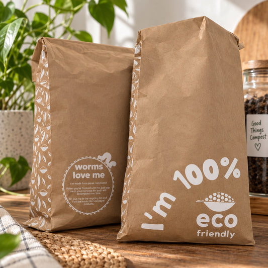 Two brown XXL kraft paper mailing bags for compostable products on a wooden table, with one bag reading 'worms love me' and the other 'I'm 100% eco friendly'.