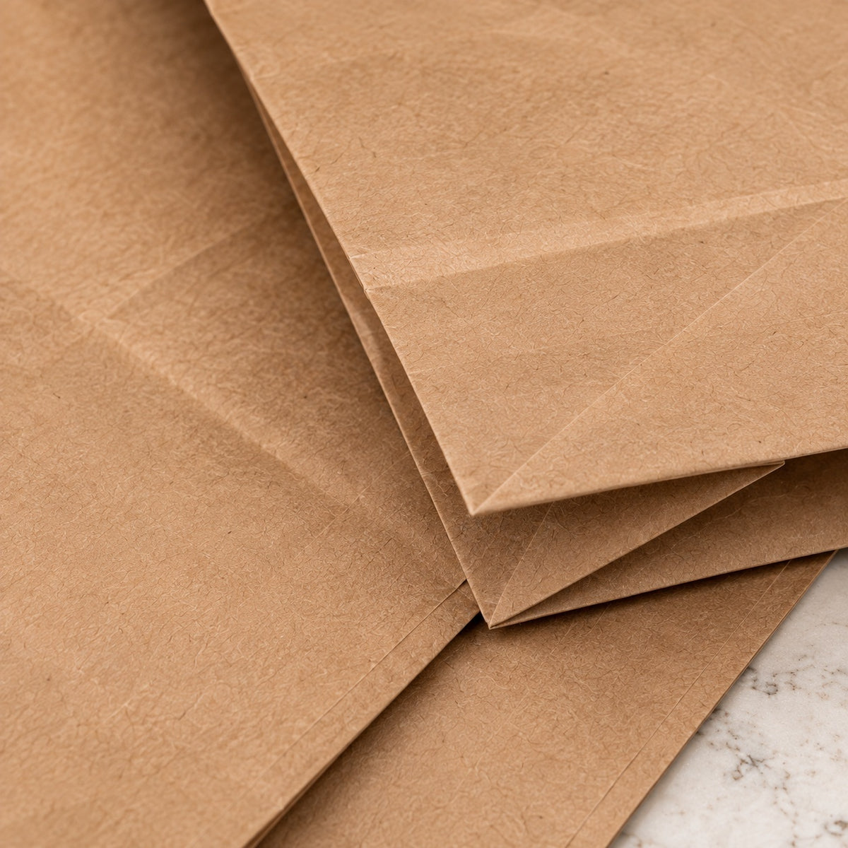 Folded brown kraft paper bags stacked on a light marble surface, showing the natural textured paper material.