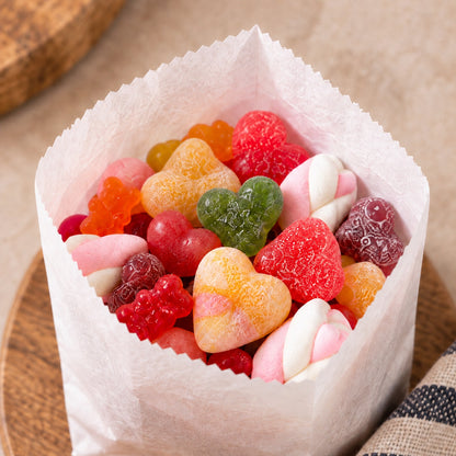 A small paper sweet bag filled with assorted colourful gummy candies, including heart-shaped gummies and marshmallow-style gummies, photographed on a neutral beige background.